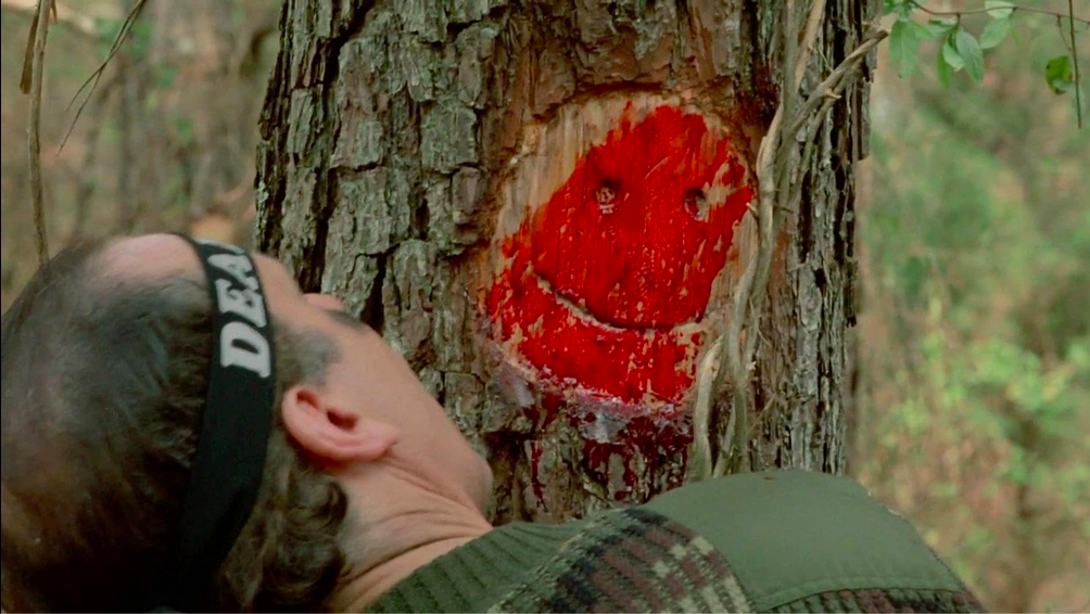 Un homme se fait écraser la tête contre un arbre, et la forme de son visage est celui d'un smiley souraint